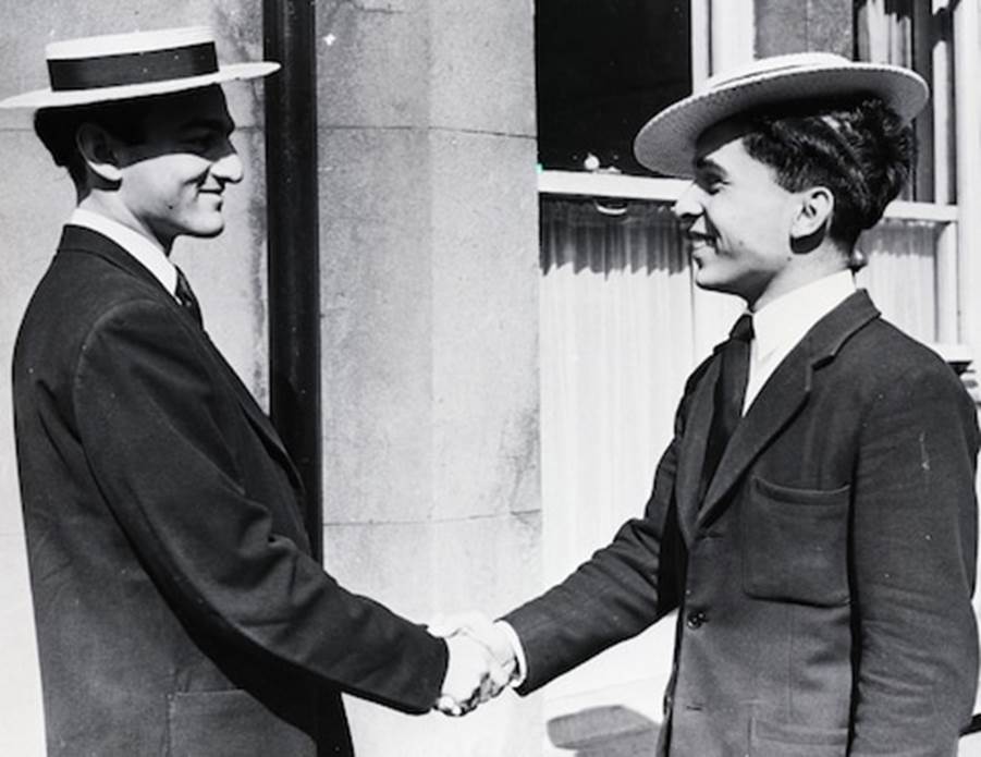 A person in a suit and hat shaking hands with another person in a suit Description automatically generated with low confidence