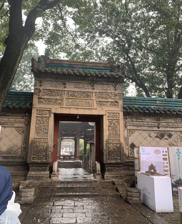 A stone building with a door and a tree Description automatically generated