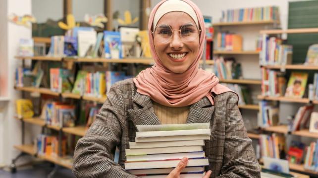 A person holding a stack of books Description automatically generated