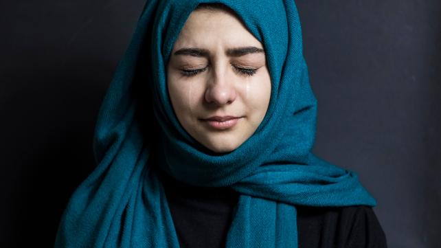 A person wearing a blue scarf crying Description automatically generated