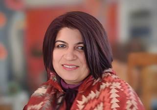 A person with dark hair wearing a red and white patterned jacket  Description automatically generated