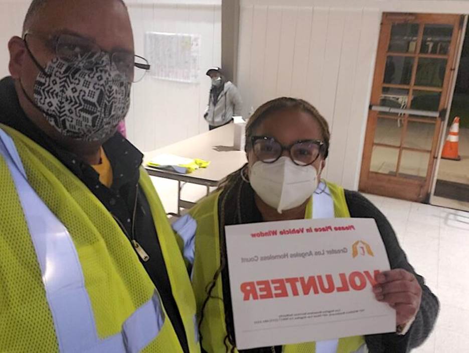 A person and person wearing masks and holding a sign Description automatically generated with low confidence