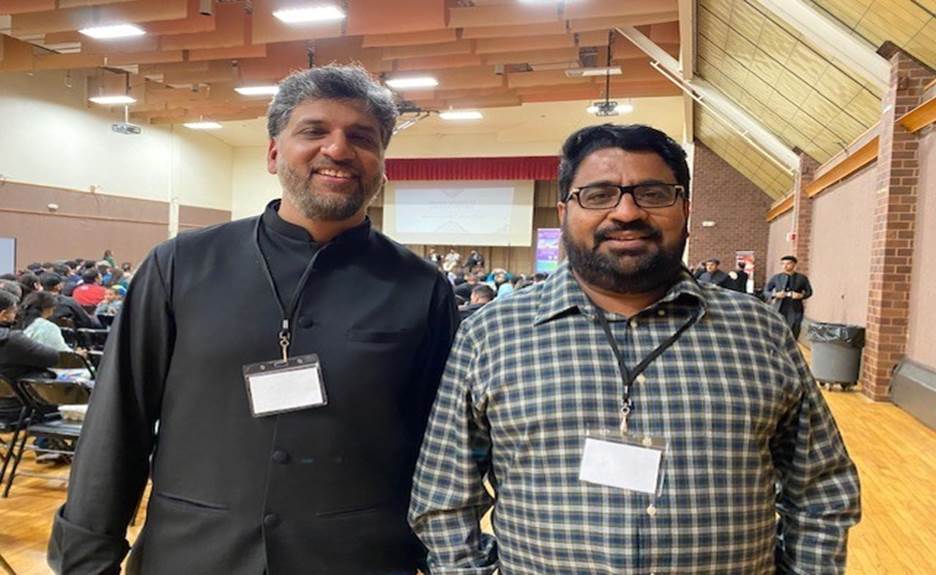 Two men standing together in a room Description automatically generated