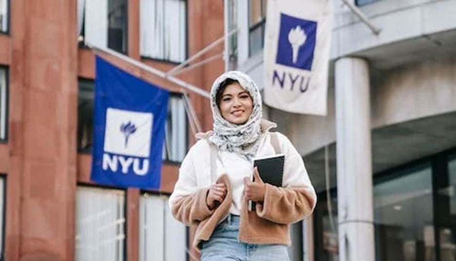 A representational image of a student standing before a universitys&nbsp;building. &mdash; Pexels