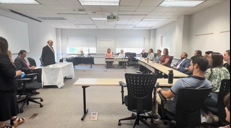 A person standing in front of a group of people in a meeting room Description automatically generated