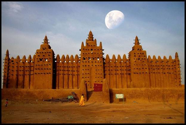 A large building with a moon in the background with Great Mosque of Djenn&eacute; in the background  Description automatically generated
