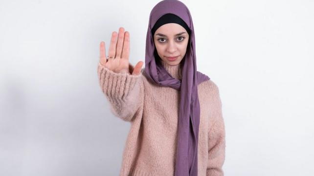 A person wearing a scarf and holding up her hand  Description automatically generated